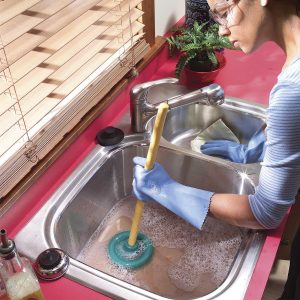Plumber Unblocking Kitchen Drain. The plumber women with a plunger unblocking kitchen drain that is clogged