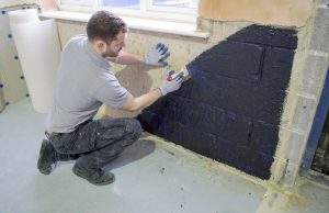Young white man damp proofing the walls.